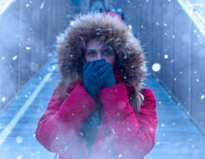 A girl with a red winter coat on with gloved hands over her mouth, with snow falling somewhare in NJ