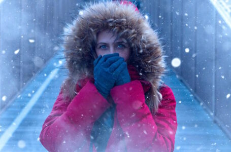 A girl with a red winter coat on with gloved hands over her mouth, with snow falling somewhare in NJ